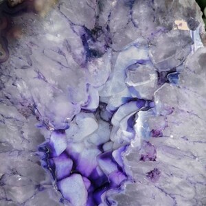 Puede incluir: Una gran geoda de &aacute;gata p&uacute;rpura y blanca con un interior forrado de cristales. La geoda est&aacute; cortada por la mitad, revelando los intrincados patrones y texturas de los cristales.