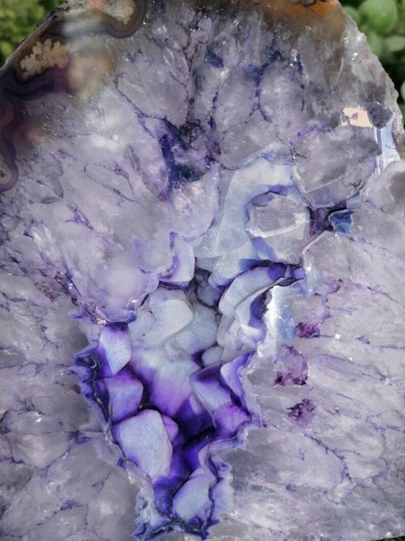Puede incluir: Una gran geoda de &aacute;gata p&uacute;rpura y blanca con un interior forrado de cristales. La geoda est&aacute; cortada por la mitad, revelando los intrincados patrones y texturas de los cristales.