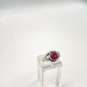 Peut inclure: Bague en argent ornée d'un grand rubis ovale. La bague présente un motif décoratif avec des volutes de chaque côté du rubis. Le rubis est d'un rouge profond et vibrant.
