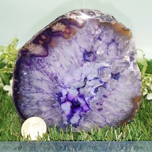 Puede incluir: Una gran rebanada de &aacute;gata p&uacute;rpura con una formaci&oacute;n de cristal blanco y p&uacute;rpura en el centro. La &aacute;gata tiene un di&aacute;metro de aproximadamente 18 cm.