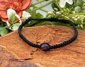 Puede incluir: Un brazalete trenzado negro con una sola cuenta redonda de amatista púrpura.