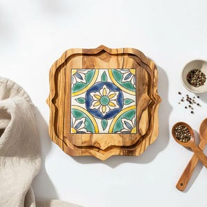 Peut inclure: Plateau de service en bois avec un insert en carreau de céramique décoratif. Le carreau présente un motif floral bleu, jaune et vert. Le plateau a un bord festonné unique. Un petit bol de grains de poivre et des cuillères en bois sont également visibles.