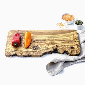 May include: A rectangular olive wood cutting board with a live edge, featuring a red and orange bell pepper. Two small white bowls hold lentils and mung beans. A gray linen cloth is draped on the side.