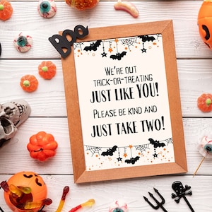 May include: A printable sign with a Halloween theme. The sign says "We're out trick-or-treating just like you! Please be kind and just take two!" The sign is surrounded by Halloween decorations, including candy corn, candy eyeballs, and a skull.