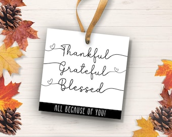 May include: A white card with black text that reads "Thankful Grateful Blessed All Because Of You!" The card has a small heart shape at the end of each line of text. The card is surrounded by fall leaves.