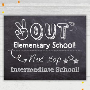 May include: Black chalkboard sign with white text that reads "OUT Elementary School! Next stop Intermediate School!" with a peace sign, a paper airplane, and stars drawn on it.