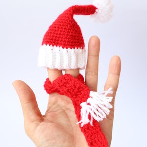 May include: A red and white crocheted finger puppet in the shape of a Santa hat with a white pom-pom on top and a matching red scarf with white fringe.