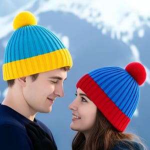 Può includere: Due berretti di maglia, uno blu e giallo, l'altro blu e rosso, ciascuno con un pompon. I cappelli sono indossati da una coppia in un ambiente montano innevato. Il cappello blu e giallo ha un pompon giallo.