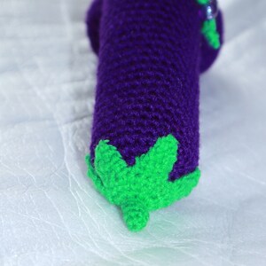 May include: Crocheted eggplant toy with a purple body and green leaves.