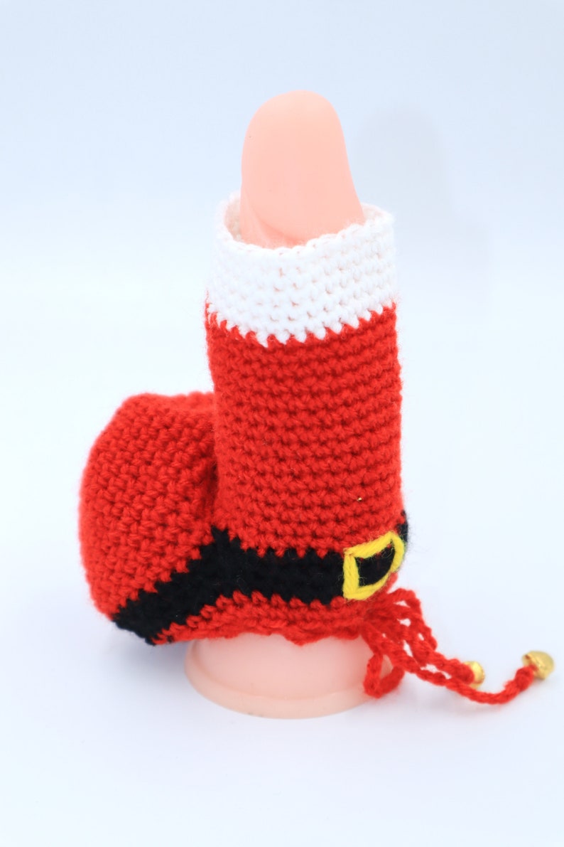May include: A crocheted Santa Claus boot with a red and white striped pattern, a black belt with a gold buckle, and a red tassel.