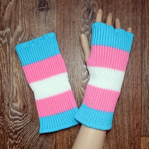 Op de afbeelding: Een paar vingerloze handschoenen in blauwe, roze en witte strepen. De handschoenen zijn gebreid en hebben een zachte, knusse textuur.