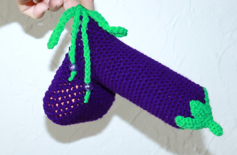 May include: A crocheted aubergine with green leaves and purple beads. The aubergine is made with a purple yarn and the leaves are made with a green yarn.