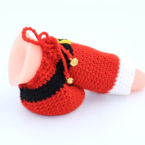 May include: A red, white, and black crocheted Santa Claus stocking with gold bells. The stocking is made of yarn and has a white cuff.