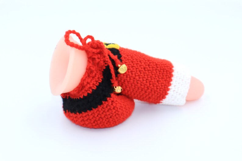 May include: A red, white, and black crocheted Santa Claus stocking with gold bells. The stocking is made of yarn and has a white cuff.