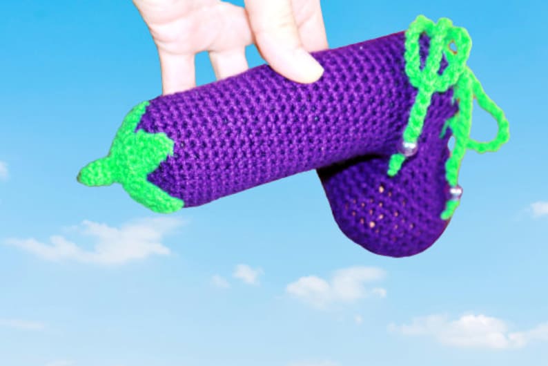 May include: A crocheted aubergine toy with green accents and beads. The aubergine is purple and has a textured surface.