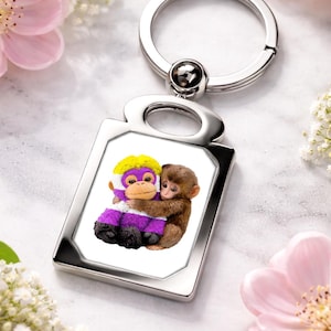 Może przedstawiać: Srebrny brelok do kluczy z prostokątną zawieszką przedstawiającą dwie przytulające się małpy z kreskówek. Jedna małpa ma fioletowe futro i żółtą głowę, druga jest brązowa. Tło zawiera różowe kwiaty i białe kwiaty.