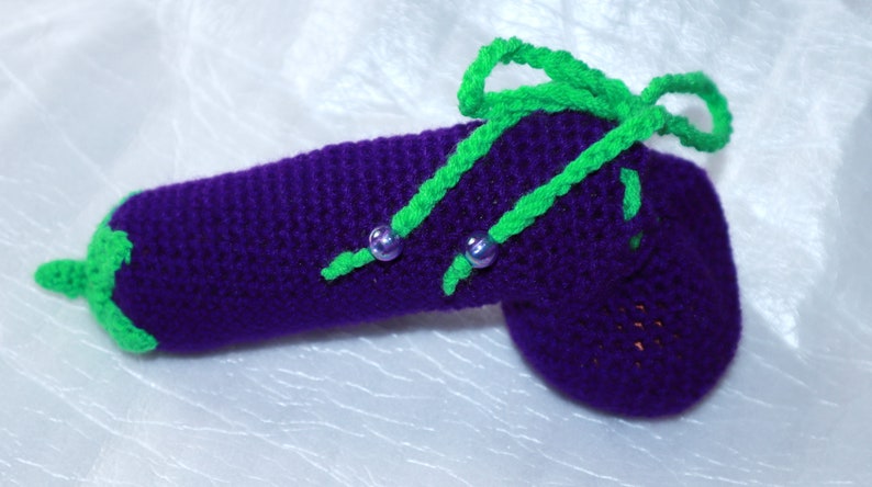 May include: A purple crocheted aubergine with green crocheted leaves and purple beads.