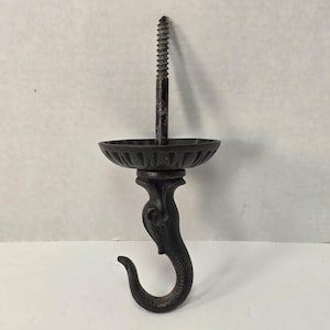 May include: A black metal hook with a screw top. The hook has a decorative design with a bowl-shaped top and a curved hook at the bottom. The screw is approximately 2 inches long.