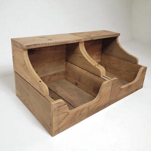 May include: A two-compartment wooden storage bin with a natural finish. The bin has a curved front and a flat top, with visible wood grain. The design is rustic and functional, suitable for organizing items.