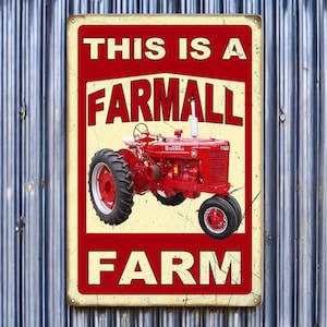 May include: A rectangular metal sign with a red and cream color scheme. The sign features a red tractor illustration and the words "THIS IS A FARMALL FARM" in bold white letters. The sign has a vintage, rustic aesthetic.