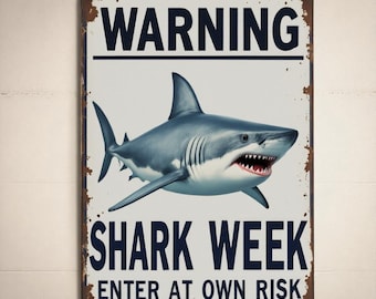 May include: A rectangular metal sign with a distressed, rusty border. The sign features a detailed illustration of a shark and the words "WARNING SHARK WEEK ENTER AT OWN RISK" in bold, dark blue letters against a white background.