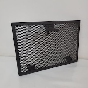 May include: Black metal fireplace screen with a mesh design and a handle. The screen has a rectangular shape and is designed to prevent sparks from escaping the fireplace.