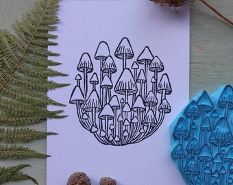 Puede incluir: Un dibujo en blanco y negro de un grupo de setas. El dibujo está sobre un fondo blanco. Hay un sello de goma azul del mismo diseño de seta en la esquina inferior derecha de la imagen.