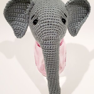 May include: A gray crocheted elephant head with black eyes, sitting on top of a pink glass jar.