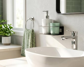 May include: A white oval vessel sink sits on a light wood vanity with a chrome faucet. A black wall-mounted shelf holds a white soap dispenser and a light green tumbler. A green patterned towel hangs from a chrome ring near a mirror.
