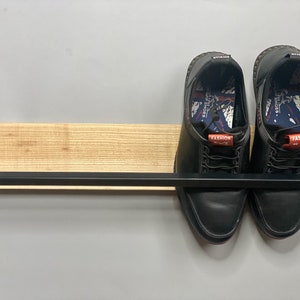 May include: A black metal shelf with a wooden top, holding two black leather shoes with red and white laces. The shoes have the word "FASHION" printed on them.