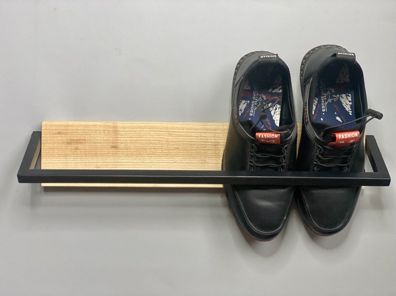 May include: A black metal shelf with a wooden top, holding two black leather shoes with red and white laces. The shoes have the word "FASHION" printed on them.