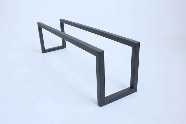 May include: A matte black metal frame featuring a rectangular, open-ended design with two parallel horizontal bars connected by two vertical U-shaped supports at each end, creating a hollow, elongated structure with clean, sharp edges.