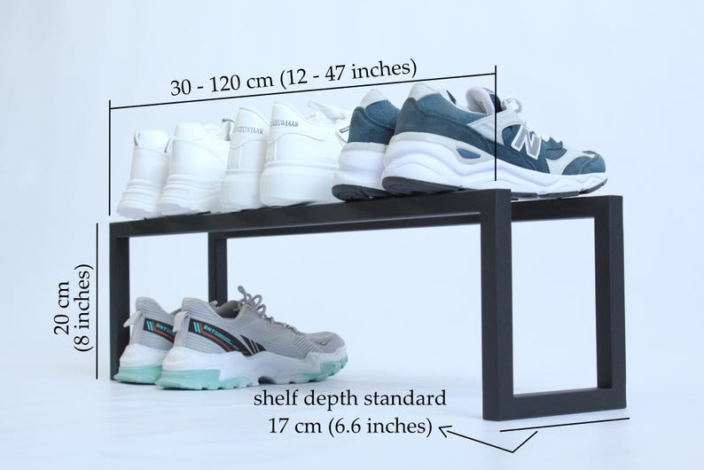 May include: A black metal shoe rack with a rectangular frame. The rack measures 30-120 cm (12-47 inches) in width, 20 cm (8 inches) in height, and has a standard shelf depth of 17 cm (6.6 inches). Several pairs of athletic trainers are displayed.