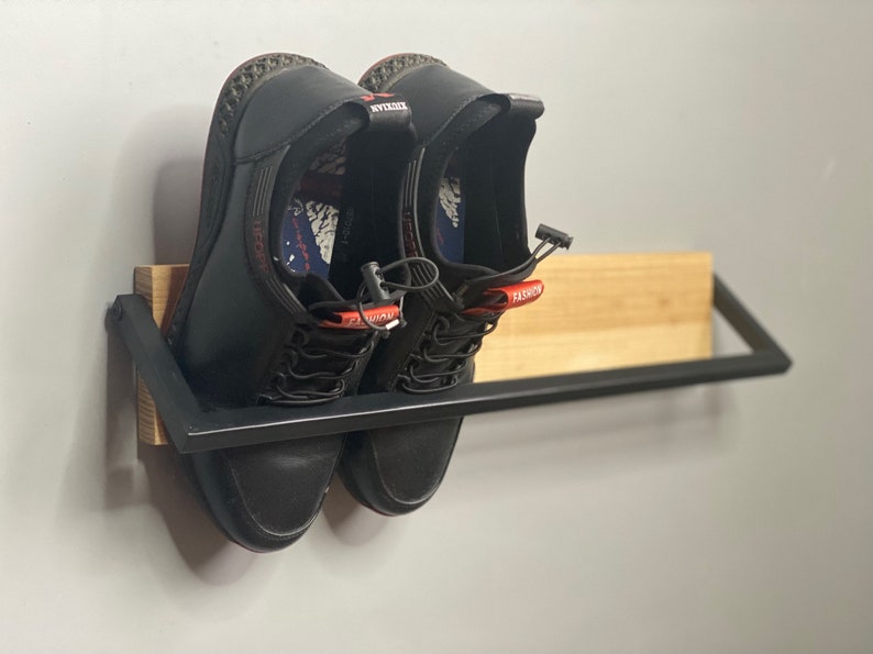 May include: A black metal shoe rack with a wooden shelf. Two black leather shoes with red accents are on the shelf.