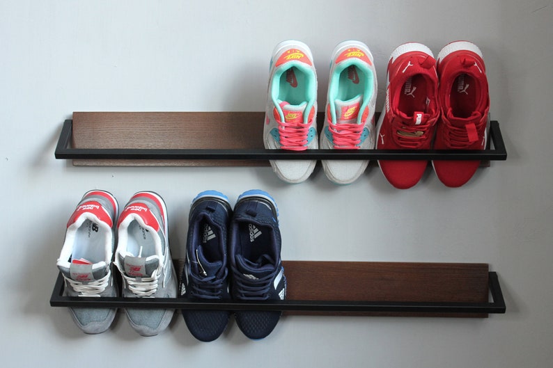 May include: Two black metal shelves with a wood grain finish, mounted on a white wall. The shelves are holding six pairs of sneakers in various colors, including red, blue, gray, and white.