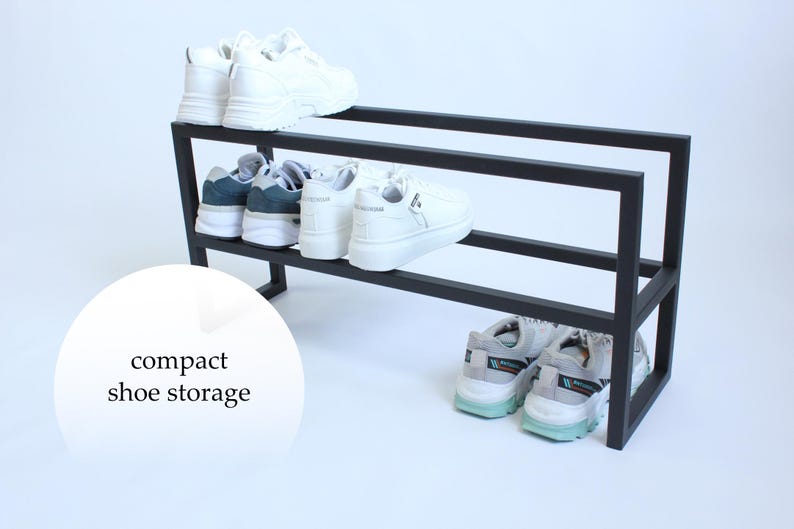Op de afbeelding: Een zwart metalen schoenenrek met twee horizontale niveaus voor het opbergen van schoenen. Het rek bevat verschillende paren sneakers, waaronder witte en grijze sportschoenen. Een cirkelvormige witte grafische overlay bevat de tekst compact shoe storage.