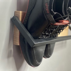 May include: A pair of black shoes with red accents and the word "UFOOP" on one shoe are hanging on a black metal shoe rack with a wooden base.