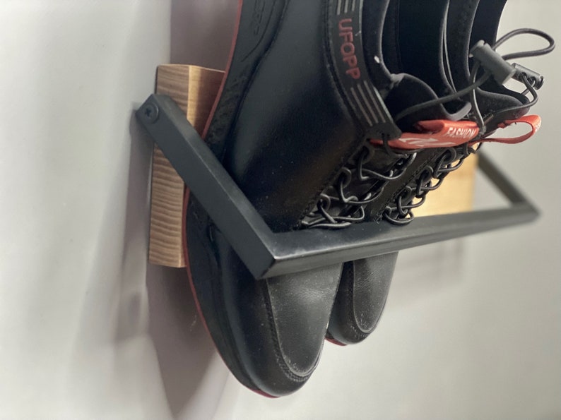 May include: A pair of black shoes with red accents and the word "UFOOP" on one shoe are hanging on a black metal shoe rack with a wooden base.