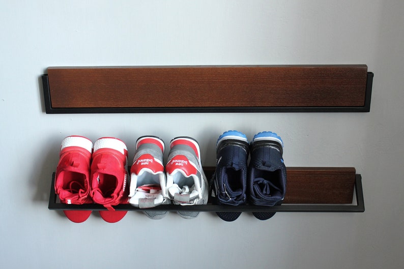 May include: A black metal shoe rack with two shelves. The top shelf is made of wood and the bottom shelf is made of metal. There are four pairs of shoes on the shelves, two pairs of red sneakers, two pairs of gray sneakers, and two pairs of blue sneakers.