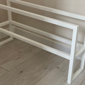 Op de afbeelding: Een wit metalen schoenenrek met een rechthoekig frameontwerp met twee horizontale niveaus. De structuur is opgebouwd uit strakke, rechte lijnen en rechte hoeken, wat een eenvoudige en functionele opbergoplossing voor schoenen biedt.