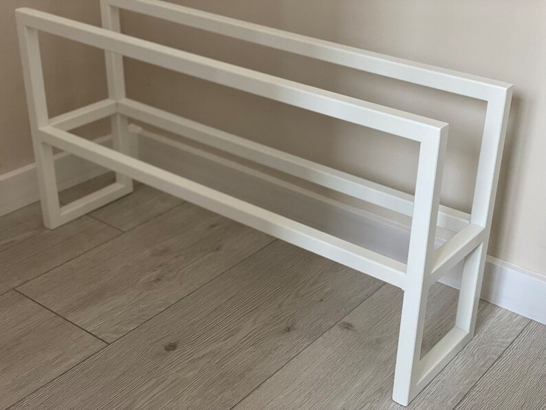 Op de afbeelding: Een wit metalen schoenenrek met een rechthoekig frameontwerp met twee horizontale niveaus. De structuur is opgebouwd uit strakke, rechte lijnen en rechte hoeken, wat een eenvoudige en functionele opbergoplossing voor schoenen biedt.