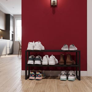 May include: A black metal shoe rack with three horizontal tiers, holding various pairs of footwear including white trainers, grey slip-ons, brown leather boots, and multi-coloured athletic shoes, organised neatly on the shelves.