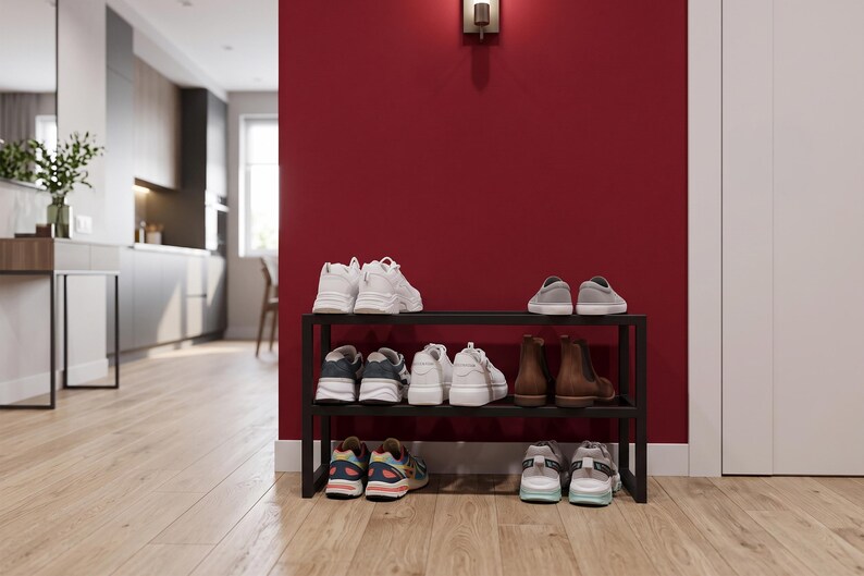May include: A black metal shoe rack with three horizontal tiers, holding various pairs of footwear including white trainers, grey slip-ons, brown leather boots, and multi-coloured athletic shoes, organised neatly on the shelves.
