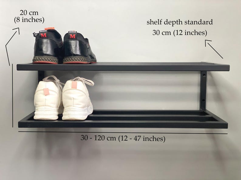 Może przedstawiać: Czarny, dwupoziomowy metalowy regał na buty montowany do ściany. Regał ma wysokość 20 cm, standardową głębokość 30 cm i szerokość od 30 do 120 cm. Para czarnych but&oacute;w sportowych znajduje się na g&oacute;rnej p&oacute;łce, a białe buty na dolnej p&oacute;łce.