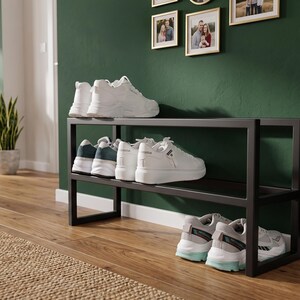 May include: A black metal shoe rack with two horizontal shelves. The top shelf holds a pair of white trainers, the middle shelf holds two pairs of white trainers, and the bottom shelf holds a pair of white trainers with light blue accents.