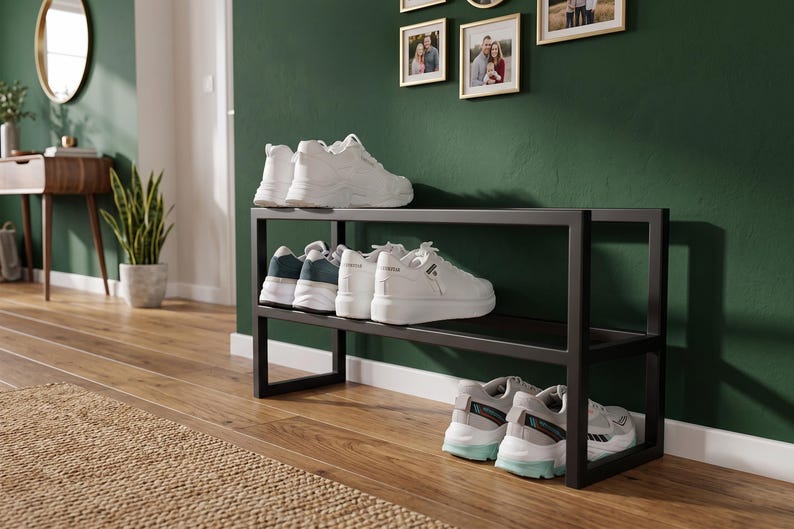 May include: A black metal shoe rack with two horizontal shelves. The top shelf holds a pair of white trainers, the middle shelf holds two pairs of white trainers, and the bottom shelf holds a pair of white trainers with light blue accents.