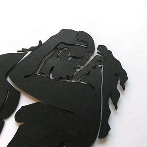 Pu&ograve; includere: Silhouette nera di due persone che si abbracciano, ritagliata dalla carta e posizionata su uno sfondo bianco.