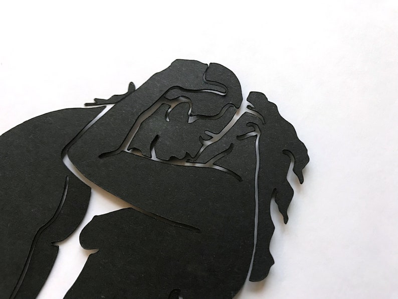 Pu&ograve; includere: Silhouette nera di due persone che si abbracciano, ritagliata dalla carta e posizionata su uno sfondo bianco.
