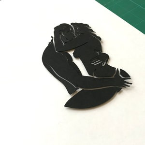 Pu&ograve; includere: Silhouette di due persone che si abbracciano, ritagliata in carta nera.