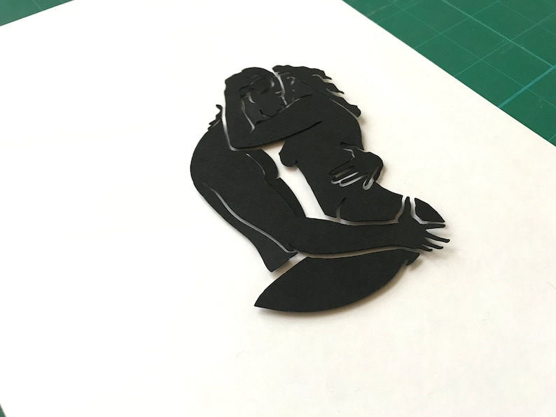 Pu&ograve; includere: Silhouette di due persone che si abbracciano, ritagliata in carta nera.